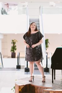 Look plus size usando vestido curto de paetê decote canoa preto e sandália de salto fino preta.