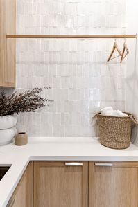 A stylish mix of classic heritage architecture and modern North American farmhouse style. Laundry room styling: Bone and Blanc Interiors, heritage home, renovation, American farmhouse, textured tiles, white tiles, white textured tiles, timber cabinetry, timber storage cabinetry, brushed bronze tap, small sink, small laundry sink, giant vase, laundry styling, woven basket, woven laundry basket, hanging rail, white benchtop, neutral home, Katie Wade Studio. Click the pin to see the full home tour!