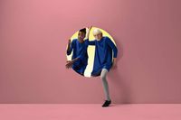 Two women peeking out of round opening in coloured wall