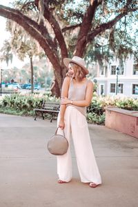 Light beige outfit for early fall with a beige sweater tank top, ivory satin pants (wide leg satin pants | ivory wide leg pants), a taupe fedora, and a grey circle bag. Light fall neutrals, chic summer to fall outfit, chic fall style, what to wear in Florida in the fall, fall Florida outfit, chic fall outfit
