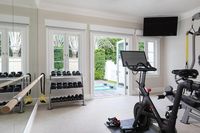 Exquisitely appointed home gym boasts a mirrored wall fitted with a ballet barre, while windows flank a glass-paneled French doors opening to the backyard.