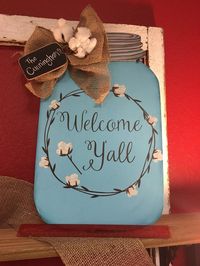 Our Mason Jar door hangers are our most popular selling item!!! We have changed it up a bit and added a new design! This wooden jar measures about 19 tall x 12 wide and is cut from 1/4 plywood. We base coat the jar in a pretty light turquoise blue color . The lettering says Welcome Yall and is a