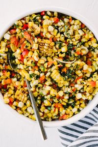 A bowl of grilled sweet corn summer salad with red bell pepper, basil, and green onions and lime honey dressing.