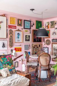 Sala de jantar integrada com parede rosa, piso de madeira, mesa de jantar redonda branca, cadeira de madeira com palhinha, pendente preto redondo, galeria de quadros, parede cheia de quadros, escultura de parede, escultura, quadro decorativo colorido, obras de arte, tapete colorido estampado, apartamento colorido, decoração maximalista, decoração colorida. Apartamento super Colorido, cheio de Arte e Garimpo | Casa de Valentina | Ph: Rafael Renzo | #decor #decoração #arch #arquitetura