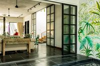 A hand-painted tropical themed wall mural matches similarly themed upholstery in the living room. Image courtesy, The Orange Lane