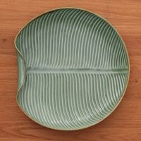 Spend $35 or more with us & shipping is FREEHandcrafted of ceramic in the shape of a banana leaf, this serving plate is sure to bring a tropical vibe to your kitchen or dining room. They work in ceramic, giving their design a textured glazed green finish.