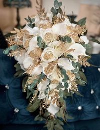 "Roses and Lillies symbolize purity, love and romance which makes this one of kind bouquet perfect for the celebration of your wedding. This stunning real touch White Gold and Green Wedding Bouquet made with the most realistic silk flowers. The gorgeous bouquet is loaded with white roses and lilies, Gold Greenery , Dark Greenery and Gold Blings The Blings are not included but can be added if needed and you can choose what color and write them in the personalized sections. The Gold Brooches Bling
