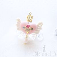 BB and B is pleased to introduce the Sailor Moon Usagi ring! Icing covers the biscuit cookie wings that extend out from the center cream of the puffed heart macaron. A crystalized moon sits at the center of the puffed heart with Swarovski rhinestones of the other Guardian members surround it. A large Swarovski pearl dangles from the bottom of the heart to add some sheen and movement to the ring.