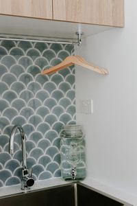It might be small on space but NOT in style! This European style laundry features a stunning blue-green fish scale or fan shape tile, timber joinery and hanging rail. Dryer stacked on top of washing machine in this compact laundry. Small space laundry renovation. Click through to the blog for all the photos and supplier details.