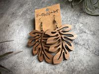 Laser cut wood earrings Wood portion measures approximately 2.25" long,2.00" wide, and 1/8" thick Available in walnut wood, cherry wood, green marbled acrylic, and gold marbled acrylic Gift box available Available hardware options are surgical brass, sterling silver, and sterling silver gold plated *This product has been carefully hand crafted; small irregularities in the surface of the materials are a natural and unique feature of the object, so it may differ slightly from the photographs in sh