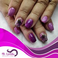 Manicura de uñas acrílicas moradas con detalle de efecto purpurina y pegatinas al agua de flores moradas.