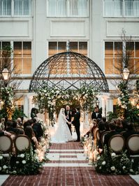 Leaf + Petal NOLA created a dream garden wedding at the Ritz Carlton courtyard in New Orleans. L+P added gorgeous neutral garden roses, ranunculus, and hydrangeas with lush greenery to the lamp posts and created beautiful hedges of garden florals to frame the aisle. Additional florals and greenery were added to the arch to frame the couple as they said their vows.