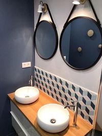 Salle de bain à l'ambiance feutrée, mur bleu orage, crédence en petits losanges, plan vasque en bois et miroirs de barbier ronds.