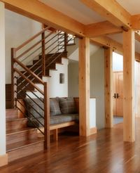 The inspiration for this built-in bench at the foot of the stairs came from the Samuel Tilton Staircase in Newport, RI by McKim, Mead & White, masters of the "Shingle Style". Built in 1881, the historic house is known for its beautiful textured surfaces and open floor plan. The timberframe, warm wood tones and richly colored fabrics in the home featured here create a welcoming space to move through or to pause and reflect. Design by MaClay Architects. Photo by Susan Teare.