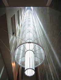 A roof-mounted heliostat (sun-tracking mirror) directs light down a 14-story atrium. The light is directed outward by a tapering tube of prismatic glass, and diffused by stretched fabric