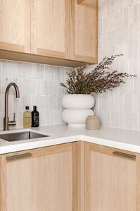 A stylish mix of classic heritage architecture and modern North American farmhouse style. Laundry room styling: Bone and Blanc Interiors, heritage home, renovation, American farmhouse, white textured tiles, timber cabinetry, timber storage cabinetry, brushed bronze tap, small sink, small laundry sink, giant vase, laundry styling, Katie Wade Studio, unique vase, curved vase, large vase with foliage, simple decor, neutral home, neutral laundry. Click the pin to see the full home tour!