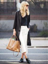 A black lace trimmed top is worn with white trousers, black oxford flats, black long blazer and a brown bag.