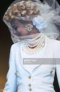 French design house Chanel shows its 1991 women's spring-summer haute couture line. Model Linda Evangelista is wearing a sheer veil and beaded necklace with a white blazer.