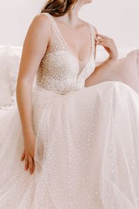Wie kleine Schneebälle funkeln die aufregenden Pünktchen des Kleides ‘Elsa’ auf sanftem Tüll. Tiefe Ausschnitte und eine herrliche Schleppe runden das Design ab und machen es zu einem aufregenden Blickfang. 💫 Gerne können wir auch noch Ärmel im Pünktchentüll hinzufügen, um dein Brautoutfit komplett zu machen!