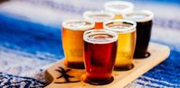 A flight of 6 different kinds of beer on a wooden paddle