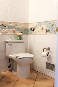 A fun, eclectic bathroom installation. This custom, handmade mosaic border wraps around the entire bathroom. Created using various glass, stone, and ceramic pieces such as mermaids, crabs, starfish, turtles, and more. A perfect fit for a nautical themed bathroom! #wetdogtileco