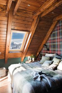 Dormitorio rústico con techo abuhardillado y pared del cabecero tapizada con tela a cuadros. #elmueble #dormitorio #rústico #casas #cabañas