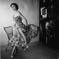 Model wearing floral dress with sash by Schiaparelli. Photographed by Henry Clarke, 1954.