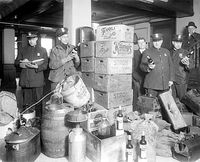 Officers admire a cache of alcohol captured during a raid. At right are a pile of suitcases, presumably used to transport the contraband throughout Detroit.