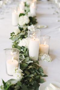 Décoration de table avec feuillage et bougies blanches dans des photophores