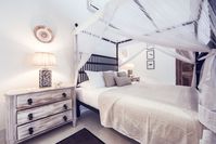 To give your white bedroom a country style charm, use distressed wood cabinets and drawers. Use light, cotton gauze curtains to cover your four-poster to complete the look. Image courtesy, Rampart Street