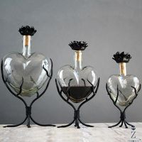 "Preserve and Serve with style and personality. Our Decanter hearts encompass the aesthetics of sculptural glass art and the delightful functions of a decanter. Each Decanter Heart utilizes a thick bottle neck for the perfect pour down to the last drop. Available in 3 sizes(Large, Medium, and Small) the voluptuously shaped hearts are all hand blown from recycled glass. Each bottle neck heart brandishes is a hand forged satin black iron flower cap and fastened to each flower cap is a custom shape