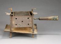 Revolutionary War Camp Stove: Wrought iron and sheet iron American camp stove used during the American Revolutionary War period. This stove retains its penny ended plate rests and curled feet, plus an early hand made wooden handle. Two splits in sheet iron ember pan. A rare survivor. (11"L front to end of handle, by 8 7/8" w x 7 1/4"H)
