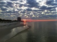 Aesthetic sunrise over the ocean, with poofy gray clouds, a beach to the left, and a highrise in the distance, in Coastal Mississippi. #aesthetic #summer