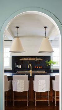 ASHLEY GILBREATH INTERIOR DESIGN: A completely remodeled kitchen designed for entertaining and everyday living. This Southern home showcases original architectural features with beautiful arch doorways and pine hardwood floors. We love the contrast of the black soapstone countertops and backsplash with the white plaster range hood and feminine touches found on the slipcover counter stools.