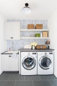 Wallpapered laundry room featuring feather wallpaper from Serena and Lily in Blue. Grey cabinets, open shelving and slate floors.
