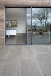 A large extension and refurbishment of a Georgian house in South Dartmoor. The natural stone walls of the house have been exposed and the interior restored. The timber clad, zinc roofed extension mirrors the Georgian house in proportions, but provides large open plan living spaces and a connection to the garden with corner glazing and sliding doors. Door Detail, with inside-outside flooring from Mandarin Stone, and larch timber cladding. Architecture, Grand Designs.