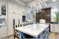 Large transitional u-shaped light wood floor kitchen with a farmhouse sink, white cabinets, white backsplash, stainless steel appliances, an island, recessed-panel cabinets, granite countertops and ceramic backsplash. #mixedcabinets #kitchendesign #traditionalkitchen #traditionaldesign #luxe #glamkitchen #whitecabinets #farmsink #farmhousesink #kitchenchandelier #islandchandelier #islandlighting #blackcountertops #tuxedokitchen
