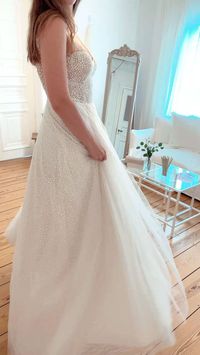Ein Brautkleid, was es so noch nicht in unserer Kollektion gegeben hat: wie kleine Schneebälle funkeln die aufregenden Pünktchen des Kleides ‘Elsa’ auf sanftem Tüll. Tiefe Ausschnitte und eine herrliche Schleppe runden das Design ab und machen es zu einem aufregenden Blickfang. Eine klassische A-Linie, die sich perfekt für deinen Hochzeitstag eignet und dich wie eine Prinzessin strahlen lässt. Dieses Design eignet sich übrigens auch besonders gut für deine Winterhochzeit.