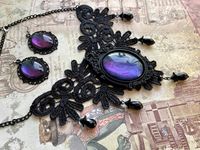 Schmuckset bestehend aus einer Statement Halskette aus schwarzer Spitze mit großem handbemaltem Glascabochon in einem Ornamentrahmen aus Kunstharz eingefasst. Zusätzlich ist die Spitze mit schwarzen Glasschliffperlen verziert. Passend dazu gibt es ein Paar Ohrrhänger mit Edelstahlohrhaken. Die Farbe des Cabochons wechselt je nach Blickwinkel die Farbe zwischen lila, blau und petrol. Der Lätzchenteil hat eine Abmessung von: ca. 14cm breit ca. 10cm hoch Ohrhänger: ca.5x3cm
