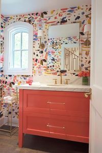 Chic, colorful, contemporary powder room boasts an orange washstand accented with brass and glass pulls and a white marble countertop fitted with a round sink with a brushed gold faucet.