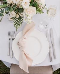 We love this simple place setting! A gorgeous scalloped-edged plate creates a whimsical, yet classic backdrop for a knotted fabric napkin. The neutral floral centerpieces and votive candles are such a lovely way to finish off a timeless setting! Photo credit: @meredithryncarz