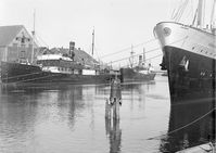 "Parti i Nidelven v/Bakke bru (uten brua) m/"Midnattsol" og "Mørejarl"" - 1937. Fotografert mot nord, rett nord for Bakke bru. Båtene i bildet er DS Midnatsol fra BDS og DS Mørejarl fra MFR. Til høyre stikker baugen fra DS Prins Olav fra NFDS inn i bildet. DS Prins Olav ligger ved Nordre Verft, som på denne tiden var eid av NFDS.