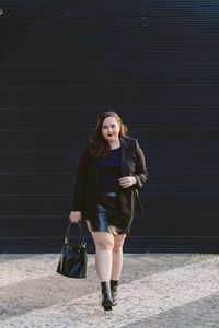 Look plus size usando blazer preto e saia de couro, bota de cano curto, bolsa bucket saco e batom vermelho