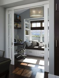 Standing past a set of white wood and glass pocket doors, this cozy study features a broad cushioned window seat over white cupboard storage. Built-in shelving and writing desk add function and save space.