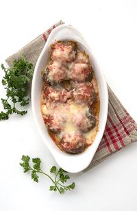 Keto Meatballs with marinara sauce, parmesan, and mozzarella in an oval dish. Top down photo on a burlap napkin with parsley beside the dish.