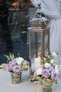 An ornate silver lantern with mercury vases of lavender and white roses.