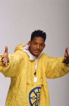a young man in a yellow jacket giving the thumbs up sign with both hands and wearing a white hoodie