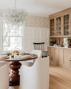A Oly Studio Muriel Chandelier Illuminates Stained Pedestal Dining Table Surrounded By White Slipcovered A Oly Studio Muriel Chandelier Illuminates Stained Pedestal Dining Table Surrounded By White Slipcovered