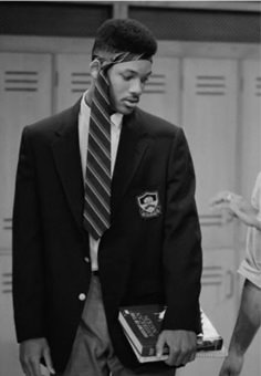 a man in a suit and tie is holding a laptop while standing next to lockers