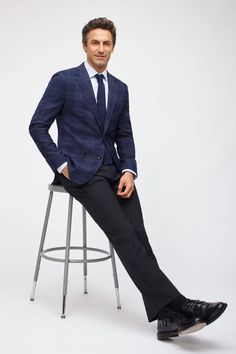 a man sitting on top of a metal stool wearing a suit and tie with his hands in his pockets
